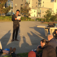 A graduate student presenting their thesis to a group of other students outside.
