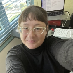 A woman with brown hair and glasses taking a selfie in an office.